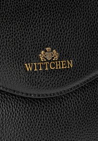 Sac en cuir noir avec une surface texturée, une marque "WITTCHEN" en or et un blason avec deux lions. Le rabat est arrondi.