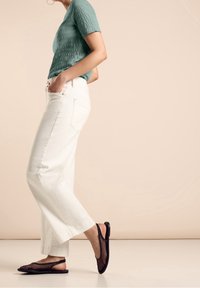 Jasnozielony top o fakturze, białe szerokie spodnie i czarne siateczkowe buty na wężyk. Prosty design, widoczne detale materiału. Neutralne tło.