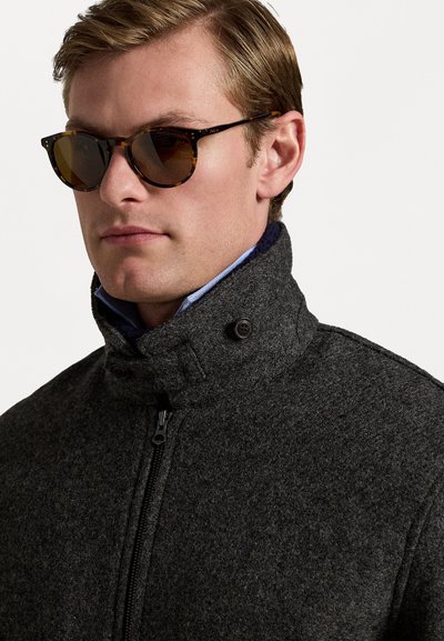 Gray wool jacket with a zippered front, high collar, and two buttons. Paired with round tortoiseshell sunglasses.