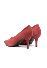 Par ženskih visokih pet dveh rdečih semiš čevljev s koničastimi prsti in tankimi petami na belem ozadju.