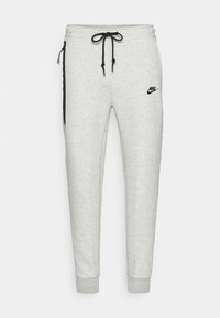 Graue Jogginghosen aus weichem Material mit einem Kordelzugbund, taillierten Beinen, schwarzen seitlichen Akzenten und einem kleinen schwarzen Logo auf der oberen linken Oberschenkelseite.