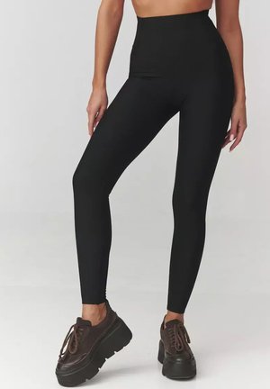 Czarne legginsy z wysokim stanem wykonane z elastycznego materiału, charakteryzujące się smukłym krojem o gładkiej fakturze, w połączeniu z masywnymi ciemnymi butami.