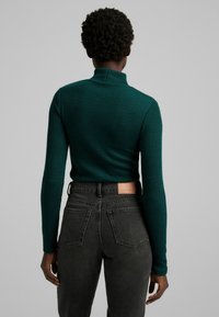 Maglione a collo alto verde a costine con maniche lunghe, abbinato a jeans grigi scuri a vita alta con tasche posteriori e una patch in pelle del marchio.