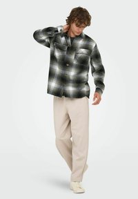 Camisa de franela de cuadros en blanco y negro de gran tamaño con dos bolsillos en el pecho, combinada con pantalones beige y zapatillas deportivas claras. Textura suave.