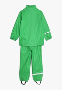 Fato de chuva verde, impermeável, com uma jaqueta de colarinho alto e punhos elásticos, combinado com calças a condizer e detalhes reflexivos.