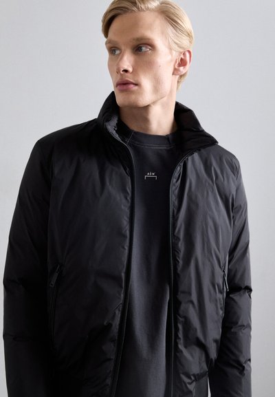 Black puffer jacket with high collar, zip closure, and two side pockets. Paired with a dark grey crewneck shirt underneath.