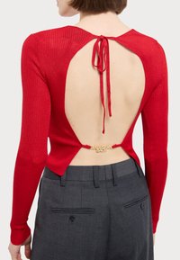 Red ribbed long-sleeve top with an open-back design, featuring a tie closure. Gold hardware detail with "EXCUSE ME, BACK" at the waist.