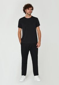 Sort crew-neck t-shirt parret med sorte bukser og hvide sneakers. Stoffet ser glat ud, og pasformen er afslappet med lige ben.