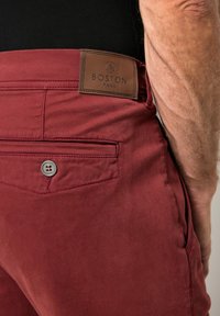 Červené bavlněné kalhoty s hladkým povrchem, obsahující koženou nášivku s nápisem "BOSTON PARK" a jedním zapínacím zadním kapsou.