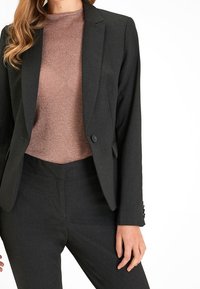 Blazer sagomato grigio scuro con rever a punta e chiusura a un bottone, abbinato a un top rosa oro lucido. Tessuto morbido, vestibilità slim.