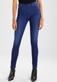 Smal jeans i mörkblått med hög midja, klassisk femfickdesign och slät yta. Parat med svarta ankelstövlar.