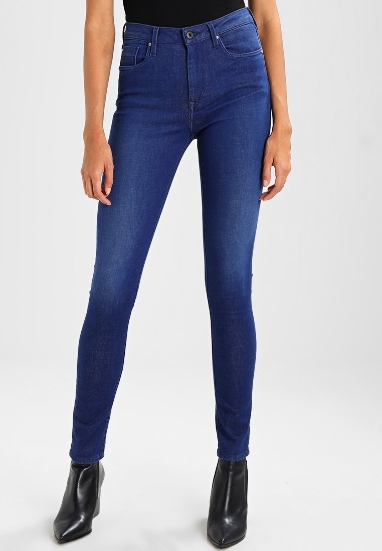 Smal jeans i mörkblått med hög midja, klassisk femfickdesign och slät yta. Parat med svarta ankelstövlar.