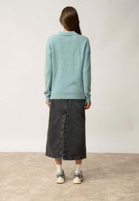 Vaaleansininen neulepaita, jossa on kauluspanta, yhdistetty mustiin farkkuhameeseen, jossa on keskilinja, ja käytetty harmaiden lenkkareiden ja valkoisten sukkien kanssa.