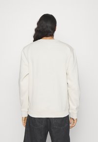 Helles beiges Sweatshirt mit langen Ärmeln, gerippten Bündchen und Saum. Weicher Stoff, minimalistisches Design und Rundhalsausschnitt; keine sichtbaren Logos oder Grafiken.