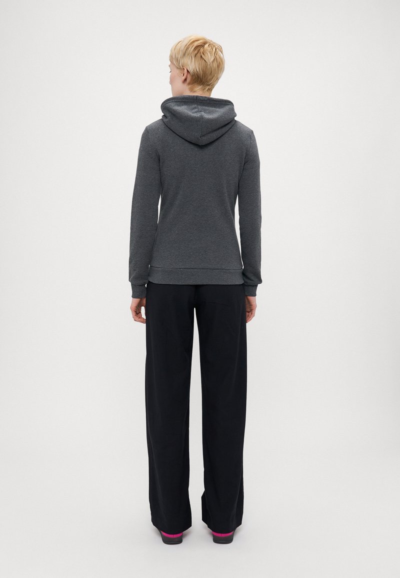 Felpa grigia con cappuccio, slim fit e maniche lunghe, abbinata a pantaloni neri larghi, con un accento rosa nella scarpa.