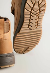 Braune strukturierte Stiefel verfügen über eine Gummisohle mit einem gemusterten Profil. Das Obermaterial besteht aus einem glatten Material mit verstärkten Nähten und Akzenten.