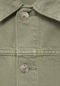 Zelena denimska srajca z ostrim ovratnikom, kovinskimi pritisnimi gumbi in vidnimi šivi po tkanini. Teksturiran zaključek.