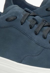 Granatowe skórzane sneakersy o teksturowanej powierzchni, z białą gumową podeszwą i czarnymi sznurówkami. Posiadają zaokrąglony czubek oraz subtelne detale przeszycia.