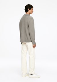 Grauer Strickpullover mit einem Kragen, kombiniert mit cremefarbenen, taillierten Hosen und weißen Turnschuhen, von hinten betrachtet.