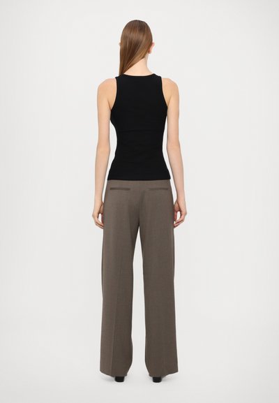Top aderente nero abbinato a pantaloni marroni a vita alta e gamba larga, con tasche posteriori e una texture liscia.