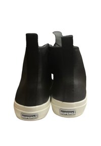 Svarta läderankelboots med en slät yta, utrustade med en vit gummisula och en logotyp på baksidan. Minimalt designade utan utsmyckningar.