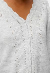 Cardigan gris clair en tissu doux, doté d'un col festonné, d'une fermeture à boutons et de motifs tricotés délicats sur le devant.