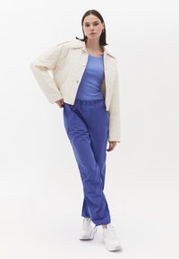 Quilted creme jakke med store knapper, blå tætsiddende top og løse blå bukser med elastisk talje; parret med hvide sneakers.