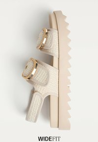 Beige plattform sandalett med vävd textur, två justerbara remmar med guldset cirkulära detaljer och en chunky zigzag-sula.