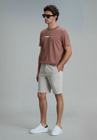 Lichtroze t-shirt met korte mouwen met de tekst "HAPPINESS", gecombineerd met lichtgrijze shorts en witte sneakers met zwarte accenten.