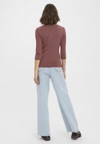 Dopasowana, bordowa bluzka z długim rękawem połączona z wysokim stanem jasnoniebieskimi spodniami w szerokim kroju oraz brązowymi, masywnymi butami. Widok z tyłu, bez widocznych logotypów.