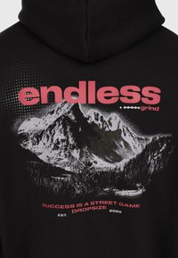 Schwarzer Hoodie mit weißer Berggrafik und rotem Text "endless grind" sowie "Success is a street game Dropsize Est. 2020" auf der Rückseite.