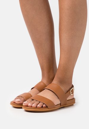 Sandales en cuir marron avec deux larges brides, une boucle à la cheville et une semelle plate, présentant un design à bout ouvert et une texture lisse.