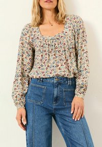 Woman wearing a long-sleeve floral blouse with a square neckline and high-waisted blue jeans with front patch pockets.