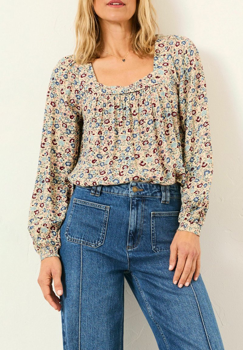 Woman wearing a long-sleeve floral blouse with a square neckline and high-waisted blue jeans with front patch pockets.