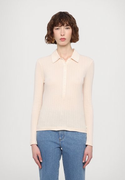 Lyserød langærmet polo med ribbet tekstur, der har en knaplukning og en klassisk krave. Båret med blå jeans.