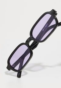 Gafas de sol rectangulares negras con lentes morados, con un marco grueso y un diseño elegante. Marca visible en el lente y la patilla.