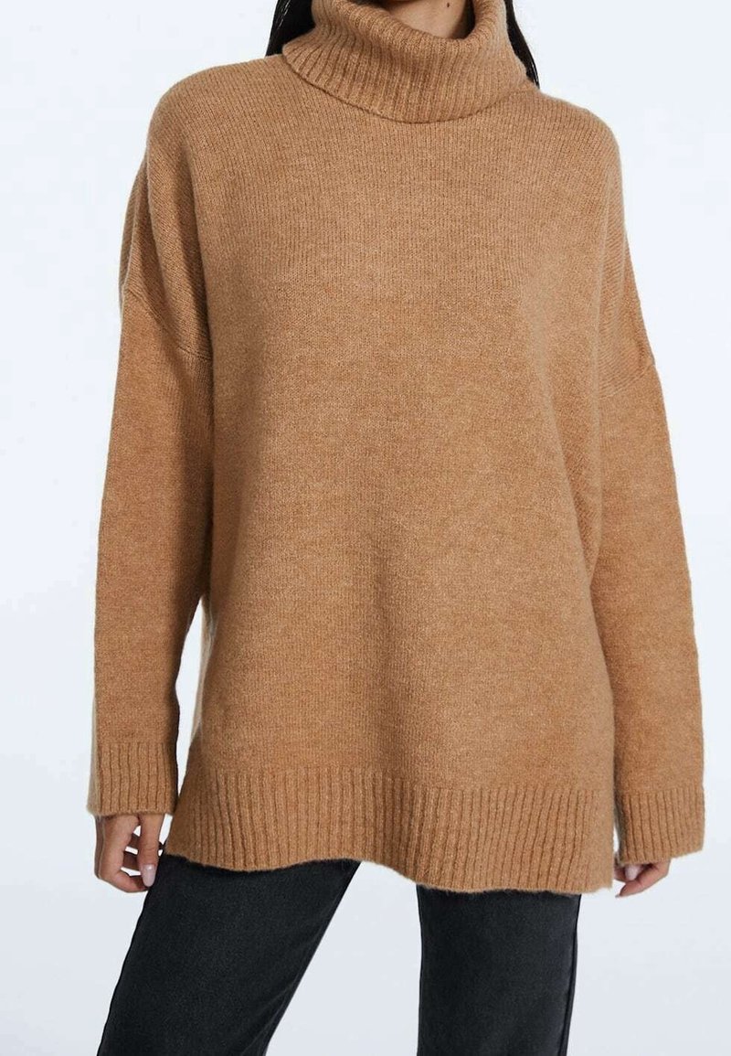 Pull à col roulé surdimensionné en tissu maille marron clair. Comprend des poignets et un ourlet côtelés, avec une texture douce et une coupe décontractée.