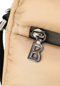 Tessuto beige di una borsa con una texture trapuntata, dotata di una cerniera nera e di un tirante in metallo argentato a forma di 'B'.