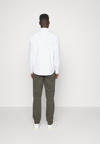 Camisa blanca de manga larga con puños abotonados, combinada con pantalones verde oliva y zapatos blancos. Vista trasera; tela suave, corte relajado.