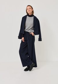 Pantalones ajustados a rayas navy combinados con un suéter gris y una chaqueta corta navy. Botines negros de tobillo completan el atuendo. Tela suave y estructurada.