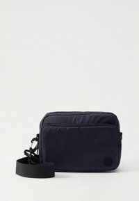 Bolso de tela azul marino para el hombro con superficie texturizada, dos compartimentos con cremallera, correa ajustable y un logo circular en el frente.