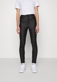 Person bär svart, högmidjade skinny byxor med knappar och vita sneakers, kombinerat med en enkel vit kortärmad tröja.