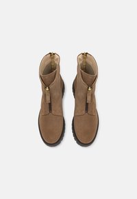 Paire de bottines marron en daim avec fermetures éclair sur le devant et semelles en caoutchouc noir, vue de dessus sur fond blanc.