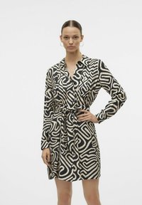 Abito camicia con un motivo a spirale nero e crema, caratterizzato da maniche lunghe, colletto e vita legata. Tessuto morbido al tatto.