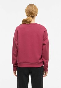 Sweat-shirt couleur baie avec une coupe décontractée, épaules tombantes et poignets côtelés. Confectionné en tissu doux, il présente un design épuré et un dos sans coutures.