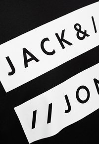 Camiseta de algodón negra con texto impreso en blanco. El diseño incluye las palabras "JACK & JON" en letras en negrita y mayúsculas sobre un fondo contrastante.