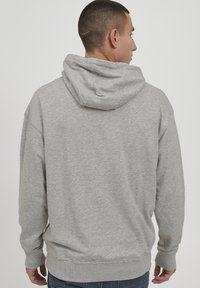 Sudadera gris hecha de una tela suave, con un bolsillo canguro frontal, capucha con cordones y puños y bajo acanalados. Diseño minimalista.
