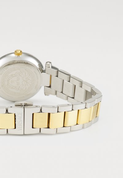 Stainless steel watch with a silver and gold-tone bracelet. Round case, textured gold crown, and engraved back featuring intricate design.