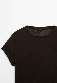 T-shirt corto a maniche corte marrone scuro con scollatura arrotondata. Realizzato in un tessuto leggero e testurizzato. Etichetta visibile all'interno della scollatura.