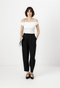 Witte off-the-shoulder top, hoge taille zwarte geplooide broek, zilveren schoudertas, zwarte schoenen. Minimalistisch ontwerp met strakke lijnen.